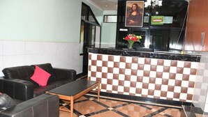 A lobby with a checkered wall, a reception desk, a black leather sofa, and a small table. - Monalisa Hotel Thika (Thika)