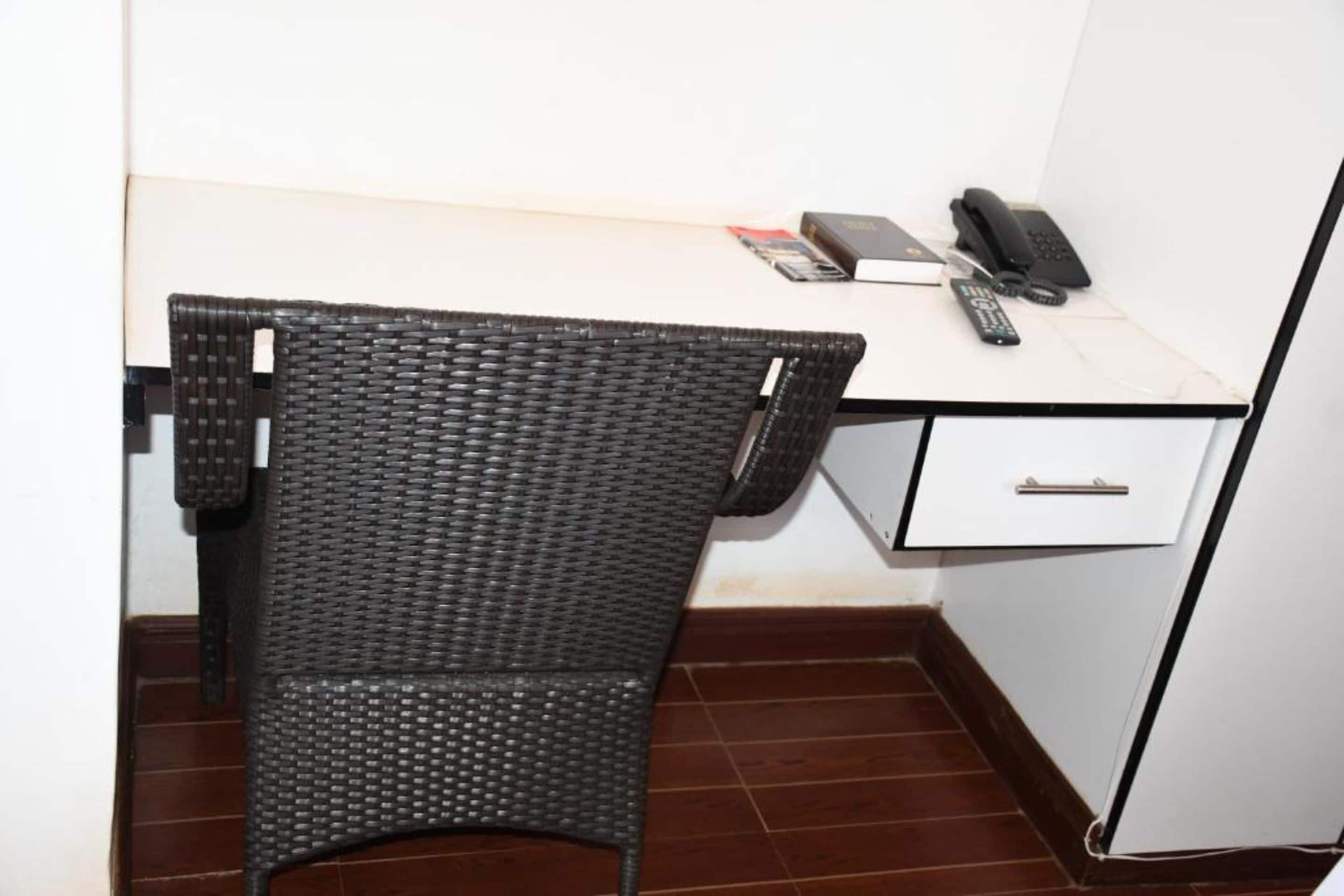 Un pequeño espacio de oficina con una silla de mimbre, un escritorio, un teléfono y un libro.