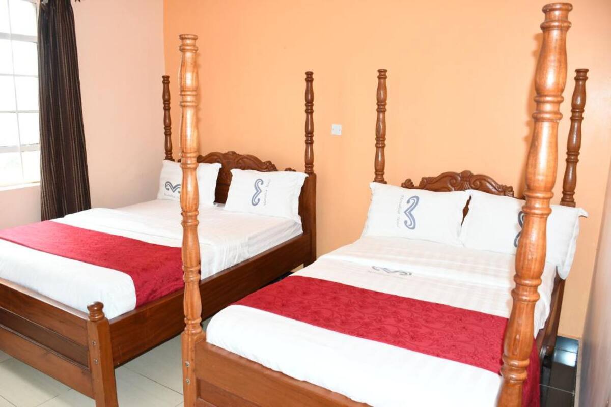 Two wooden four-poster beds with white linens and red blankets, positioned against an orange wall.