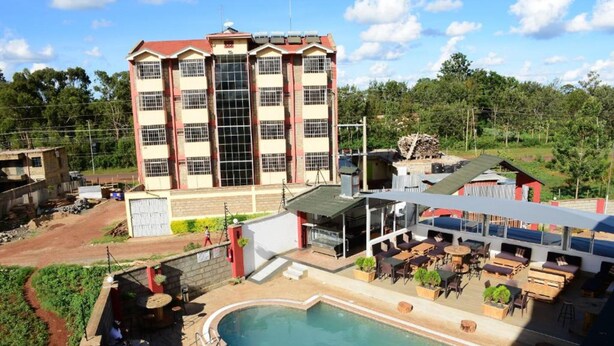 A hotel with a swimming pool, outdoor seating area, and a large building in the background. - Monalisa Hotel Thika (Thika)