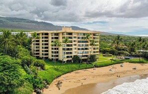 Ein mehrstöckiges Hotel mit flachem Dach, umgeben von üppiger Vegetation und einem Strand.