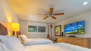 Une chambre d’hôtel avec deux lits, un ventilateur de plafond, une grande télévision et une fenêtre avec des stores.