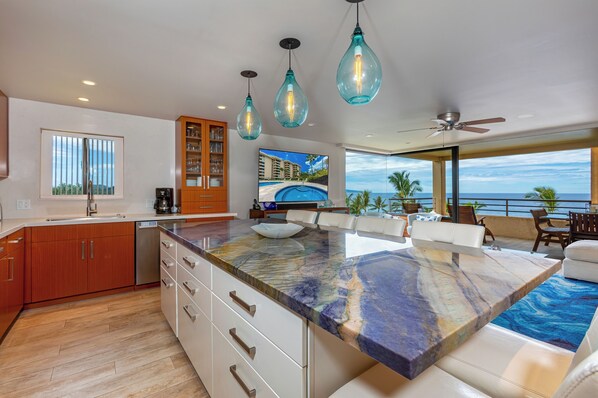 A modern kitchen with a large island, wooden cabinets, and a view of the ocean.