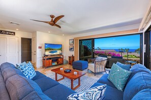 Una sala de estar moderna con un televisor grande, asientos cómodos y vista al océano.