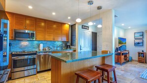 Una cocina moderna con armarios de madera, una isla grande con taburetes, electrodomésticos de acero inoxidable y un salpicadero azul.
