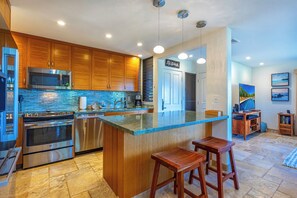 Una cocina moderna con armarios de madera, una isla grande con taburetes, electrodomésticos de acero inoxidable y un salpicadero azul.