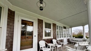 A covered porch with white wicker chairs and tables, wooden siding, and a door with glass panels. - Charming home in downtown Chatham (Chatham)