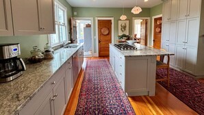 A modern kitchen with granite countertops, a central island, and a patterned rug. - Charming home in downtown Chatham (Chatham)