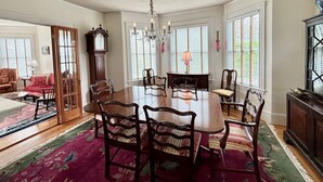 A dining room with a large wooden table, six chairs, a chandelier, and a clock. - Charming home in downtown Chatham (Chatham)