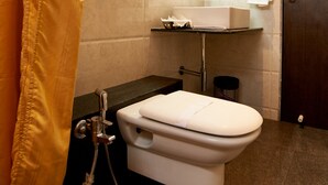 A bathroom with a toilet, a shower, and a shelf with toiletries. - Hotel Sai Nisarg (Rahata)