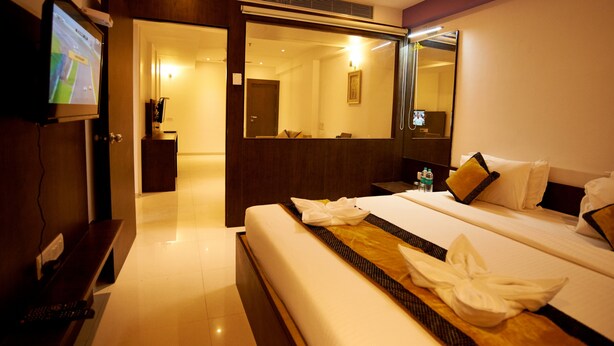 A hotel room with a bed, bedside table, and a TV mounted on the wall. - Hotel Sai Nisarg (Rahata)
