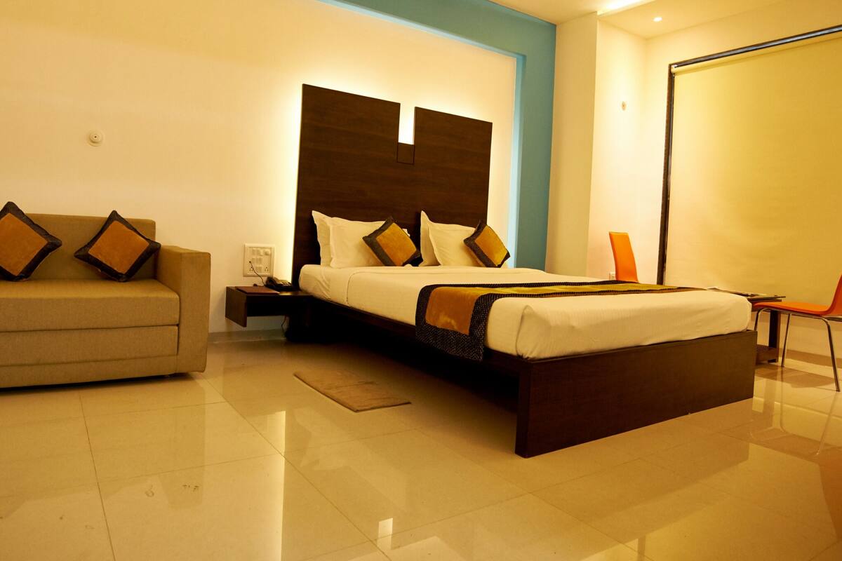 Una habitación de hotel con cama, sofá, mesita de noche y silla.