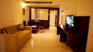 A living room with a sofa, coffee table, TV, and a dining area with chairs and a table. - Hotel Sai Nisarg (Rahata)