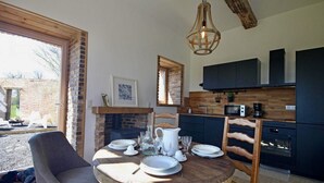 A cozy kitchen with a round wooden table set for dining, a dog lying outside, and a rustic ceiling light. - The Château Orangerie (Hugleville-En-Caux)
