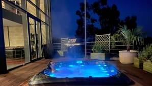 Ein Whirlpool auf einer Holzdielen-Terrasse mit Glasumrandung und Gartenmöbeln.