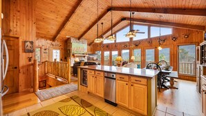 A spacious kitchen with wooden cabinets, a large island, and a view of the outdoors through large windows. - Amazing 5 br cabin-amazing mtn views & mins to NP (Sevierville)