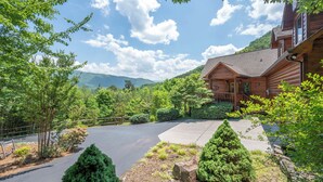 A log cabin with a paved driveway, surrounded by lush greenery and mountains in the background. - Amazing 5 br cabin-amazing mtn views & mins to NP (Sevierville)