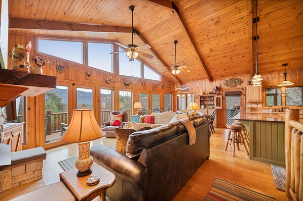 A spacious cabin with a large living area, wooden ceiling, and large windows offering views of the outdoors.