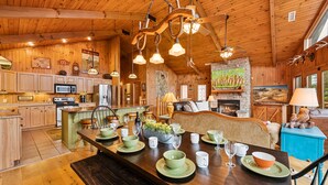 A wooden cabin interior with a dining area set for a meal, a kitchen with modern appliances, and a fireplace. - Amazing 5 br cabin-amazing mtn views & mins to NP (Sevierville)