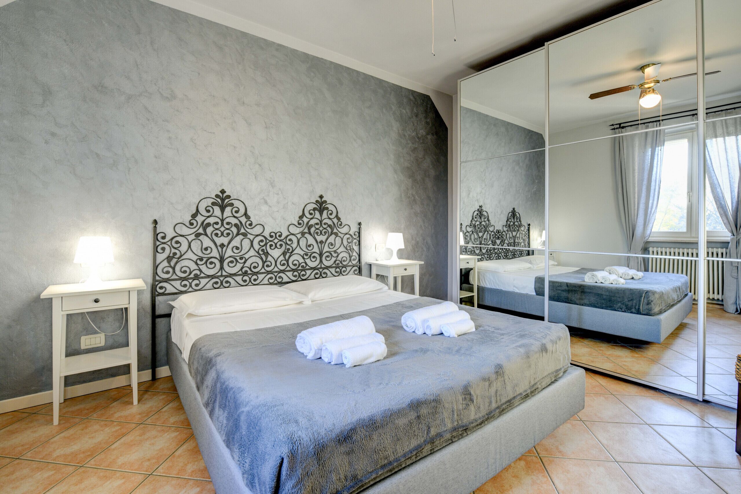 A modern bedroom with a large bed, a bedside table, a nightstand, a mirror, and a ceiling fan.