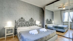 Une chambre à coucher moderne avec un grand lit, une table de chevet, une commode, un miroir et un ventilateur de plafond.