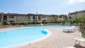 Une piscine entourée de chaises longues, elle-même bordée d’immeubles à plusieurs étages dotés de balcons.