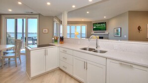 Una cocina moderna con armarios blancos, una isla grande con fregadero y una zona de comedor con mesa y sillas.