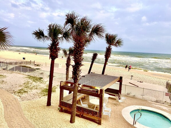 A beachside pool area with a wooden deck and chairs, surrounded by palm trees and a view of the ocean.