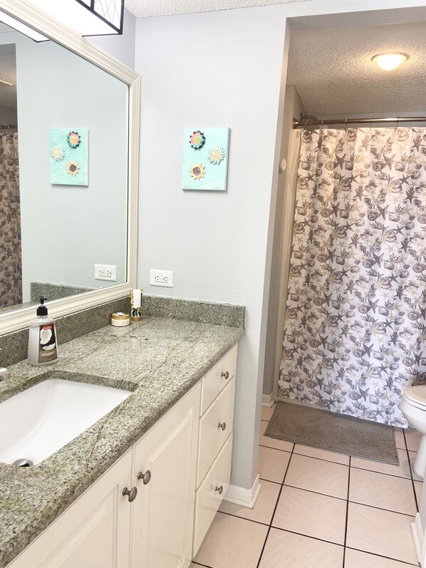 A bathroom with a granite countertop, a white sink, a mirror, two wall-mounted flower art pieces, and a shower curtain with a starfish pattern. - OCEAN VIEW~GREAT REVIEWS~Family friendly Gulf front with heated pool. (Gulf Shores)