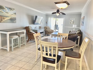 A dining area with a round table and four chairs, a sofa, a television, and a ceiling fan.