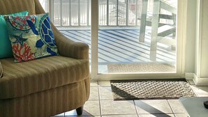 Une chambre avec vue sur la plage, une chaise avec un coussin, une lampe et une porte donnant sur une terrasse extérieure.