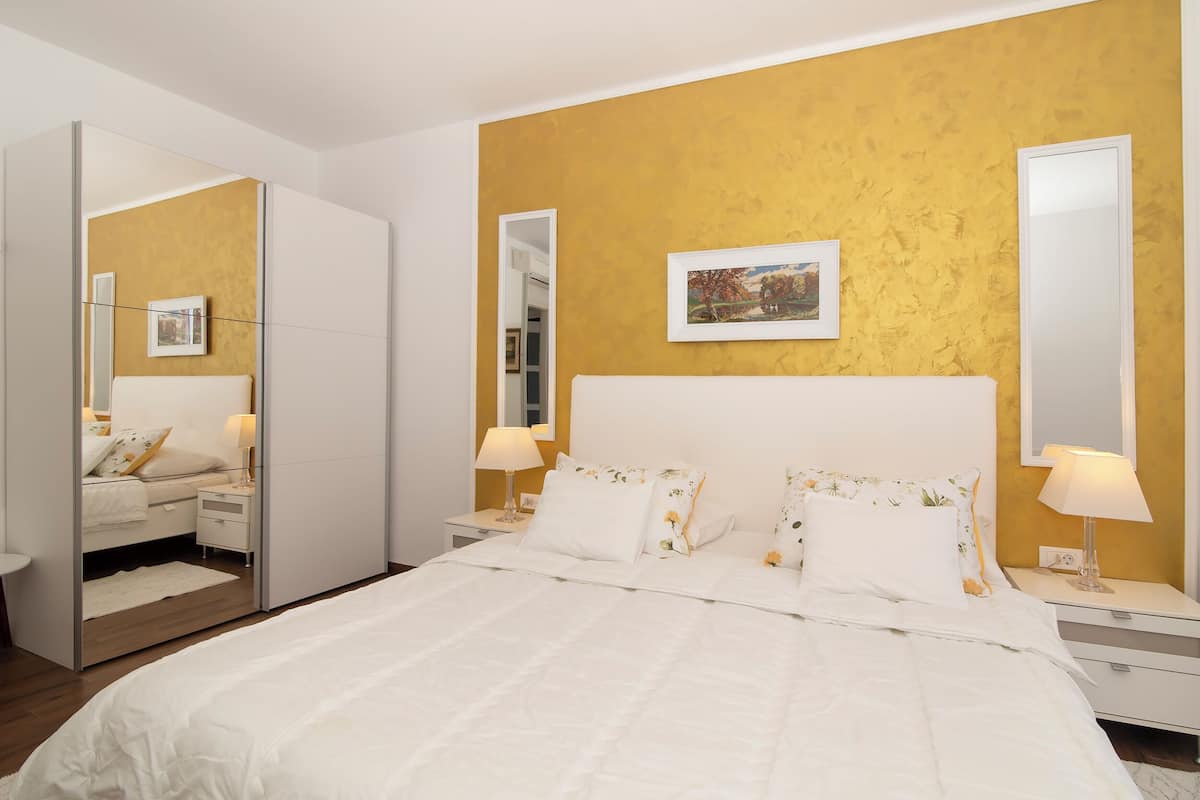 A bedroom with a bed, bedside tables, a mirror, and a picture on the wall.