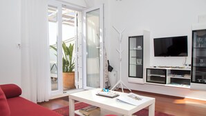 Una sala de estar moderna con un sofá rojo, una mesa de centro blanca y un gran ventanal con vistas a plantas y un balcón.