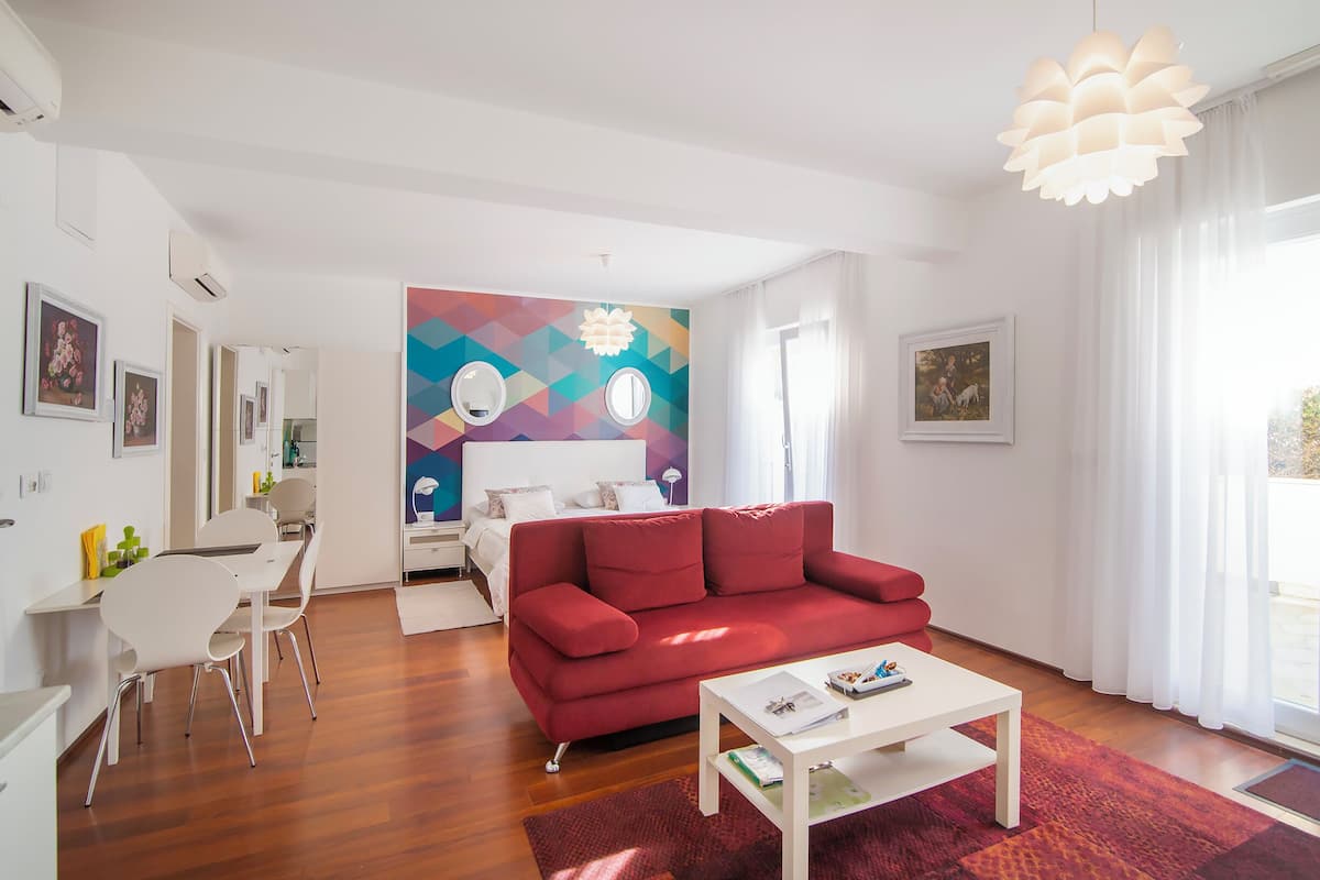 A modern living room with a red sofa, white coffee table, and a colorful geometric wall mural.