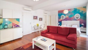 Una sala de estar moderna con un sofá rojo, una mesa de centro blanca y una cocina con armarios blancos y un mural de colores.