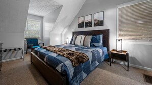 A bedroom with a sloped ceiling, a bed with a blue quilt, a wooden headboard, and three framed pictures on the wall.