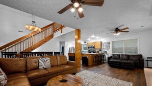 A spacious living area with a brown leather sofa, a wooden coffee table, and a staircase with wooden railings leading to an upper level.