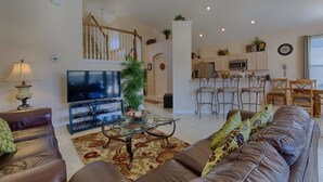 A spacious living room with a large flat-screen TV, a glass coffee table, and a brown leather sofa. A staircase leads to an upper level. - Resort 5 Bed Private Pool & Spa, Game Room Home 5 Bedroom Villa by RedAwning (Kissimmee)