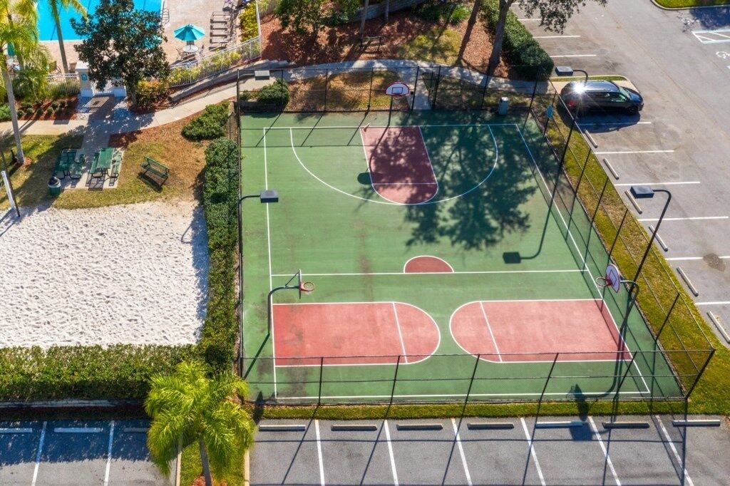Luchtbeeld van een basketbalveld met een omrastering, een parkeerplaats en een zwembad.