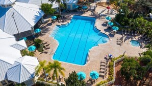 A swimming pool with lounge chairs and umbrellas, surrounded by palm trees and a building with a unique roof design. - 4 Bedroom/3 Bath South Facing Pool/Spa Villa 4 Villa by RedAwning (Kissimmee)