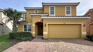 A two-story house with a yellow facade, a garage, and a brick driveway. - Veranda Home, 8br, 6 En-suites, Lake View,pool/spa 8 Bedroom Villa by RedAwning (Kissimmee)