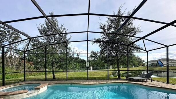 A covered outdoor swimming pool with a brick deck, surrounded by a metal fence and trees. - Veranda Home, 8br, 6 En-suites, Lake View,pool/spa 8 Bedroom Villa by RedAwning (Kissimmee)