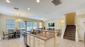 A spacious kitchen with a large island, a dining area with a table and chairs, and a staircase leading to another level. - Veranda Home, 8br, 6 En-suites, Lake View,pool/spa 8 Bedroom Villa by RedAwning (Kissimmee)