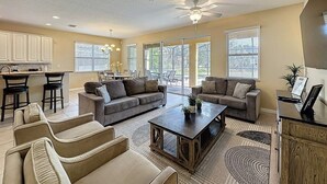 A spacious living room with a large sofa set, a coffee table, and a dining area with bar stools. - Veranda Home, 8br, 6 En-suites, Lake View,pool/spa 8 Bedroom Villa by RedAwning (Kissimmee)