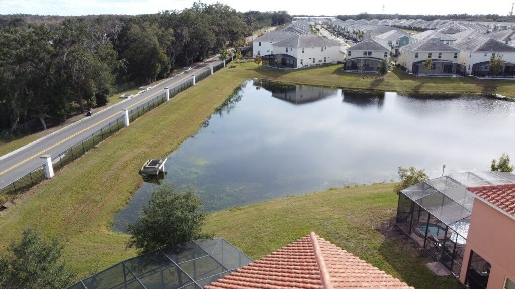 A residential area with a large pond, houses with sloped roofs, and a road running parallel to the pond.