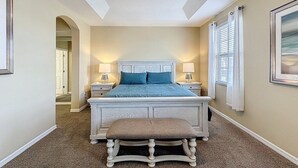 A bedroom with a large bed, two bedside tables, a bench, a ceiling fan, and a door leading to another room. - Veranda Home, 8br, 6 En-suites, Lake View,pool/spa 8 Bedroom Villa by RedAwning (Kissimmee)