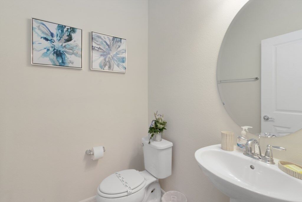 A bathroom with a toilet, sink, and two framed abstract paintings on the wall.
