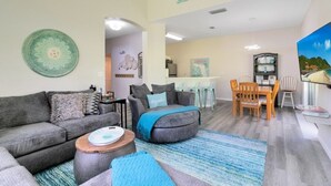 A living room with a sofa, ottoman, and coffee table, a dining area with a table and chairs, and a kitchen in the background. - Disney Area 4 Bed Emerald Island 4 Bedroom Townhouse by RedAwning (Kissimmee)