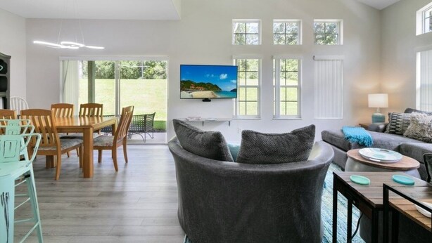 A spacious living area with a grey sofa, a dining table with chairs, and a TV mounted on the wall. - Disney Area 4 Bed Emerald Island 4 Bedroom Townhouse by RedAwning (Kissimmee)