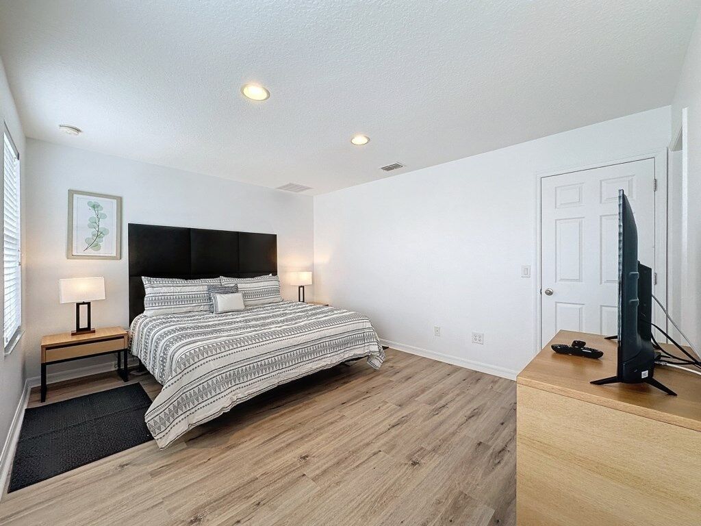 A bedroom with a bed, bedside tables, a desk, a television, and a door.